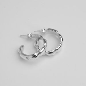 Picture shows Danaë earrings product on white background. Side view. One earring is on top of the other. Both laid facing the left side Hoop earrings with approx. 1.5cm diameter. On the surface of the hoop are four deep inserts. The hoop is approx. 4mm wide.