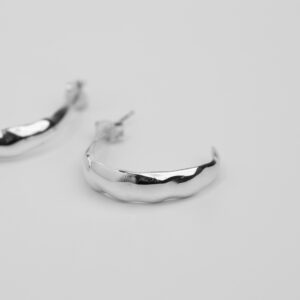 The picture shows iris hoop earrings on white background. Iris hoops are recycled silver hoops of approximately 3cm diameter. The width of the hoop is approx. 6mm and is wider at the middle compared to the ends that is creating an edge. In the picture one hoop is shown front view and the other is half shown on the left side of the image.